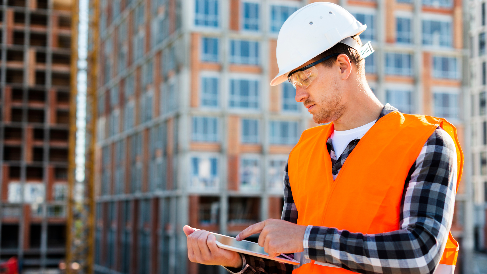 Consultant at a property wearing an orange high-vis vest, white hard hat and holding an iPad.
